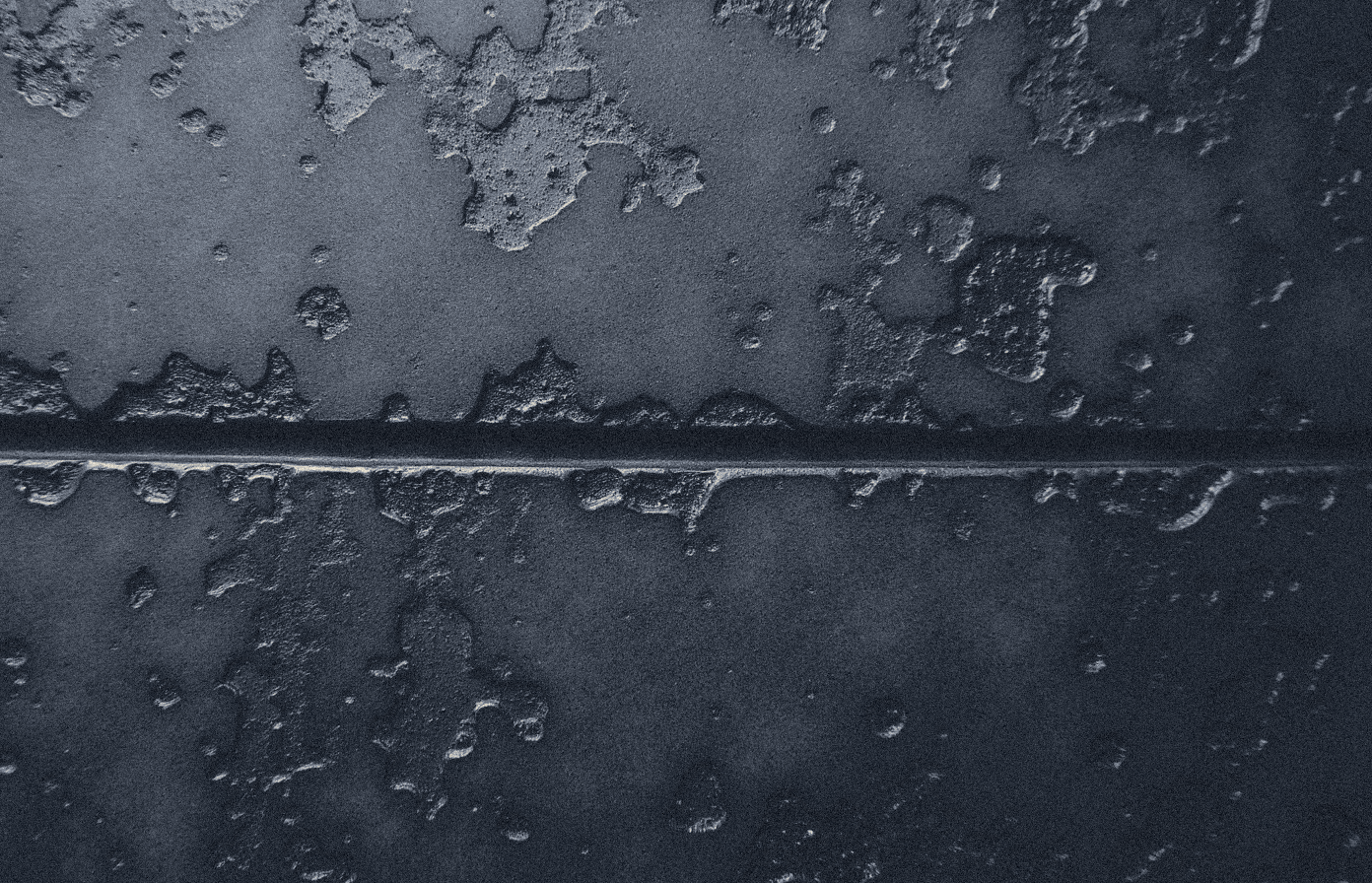 Extreme macro of an ancient cast bronze surface, mottled verdigris and dark patina, a single casting seam crossing the frame under raking light.
